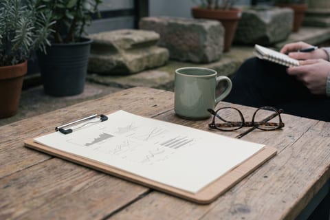 A clipboard, a coffee cup and a pair of glasses on a desk